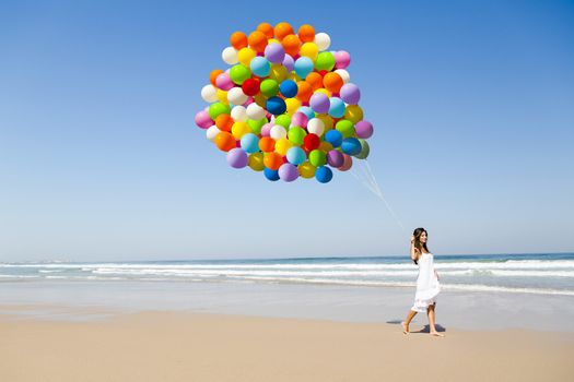 Beautiful girl walking in the beach holding dozens of colored balloons