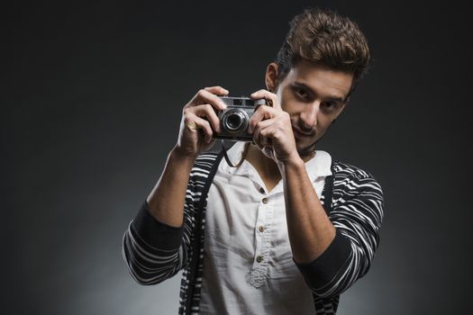 Studio portrait of a fashion young man posing with a old photographic camera, over a dark background