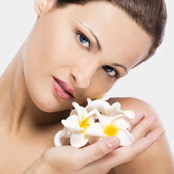 Close up portrait of a beautiful blonde woman holding plumeria flowers close to the face