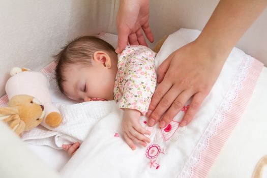 Hands of mother caressing her cute baby girl sleeping in a cot with pacifier and stuffed toy