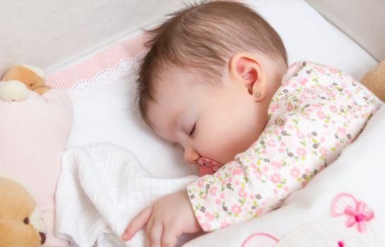 Portrait of cute baby girl sleeping in a cot with pacifier and stuffed toy