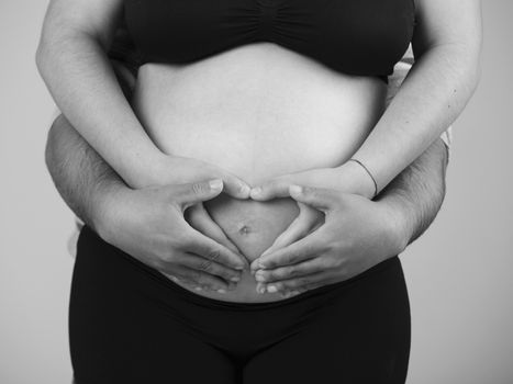 Future parents making a heart with hands on the belly, over a gray background