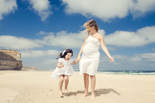 Beautiful pregnant woman and her little daughter playing on the beach