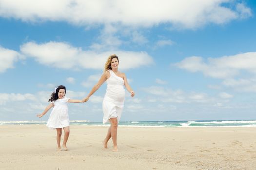 Beautiful pregnant woman and her little daughter walking on the beach