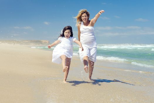 Beautiful pregnant woman and her little daughter really happy playing on the beach