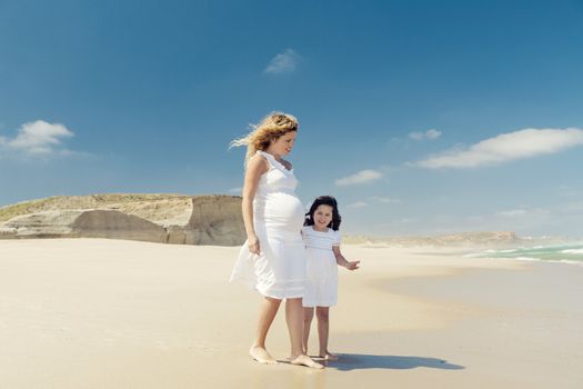 Beautiful pregnant woman and her little daughter on the beach