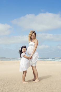 Beautiful pregnant woman and her little daughter on the beach