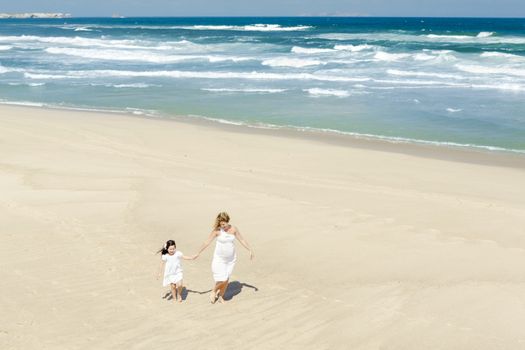 Beautiful woman and her little daughter walking on the beach