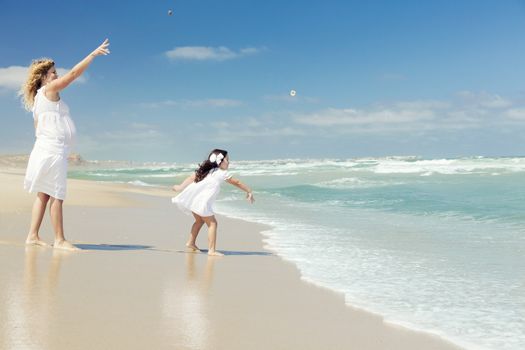 Beautiful pregnant woman and her little daughter throwing stones on the beach