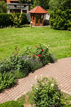 Beautiful garden with blooming roses, brick path and a small gazebo