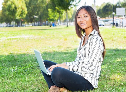 Pretty asian girl on laptop sitting on the grass