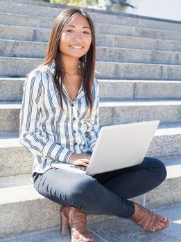 Smiling asian girl sitting on stairs and using a laptop