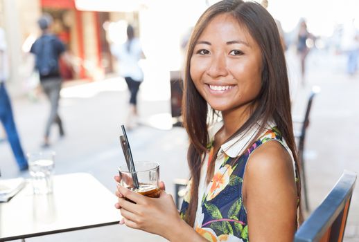 Close up portrait of a smiling asian girl drinking a soda sitting on terrace