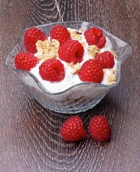 Delicious Dessert with Fresh Ripe Raspberries, Muesli and Dairy Cream in Glass Bowl isolated on Wooden background