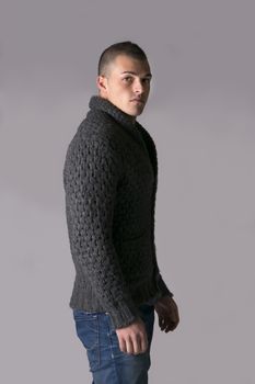Attractive young man with wool sweater and jeans, isolated on grey background