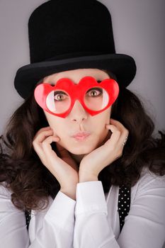 Portrait of a beautiful girl wearing heart-shaped glasses and black top hat.