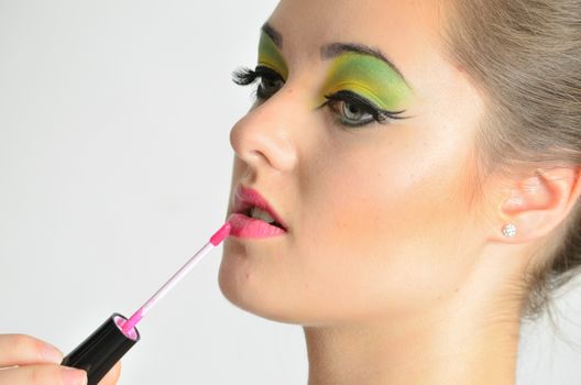 Portrait of young Polish female. Teenage girl with colorful makeup using lip gloss on her lips.