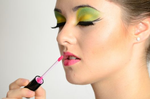 Portrait of young Polish female. Teenage girl with colorful makeup using lip gloss on her lips.