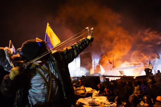 KIEV, UKRAINE - January 24, 2014: Mass anti-government protests in the center of the Ukrainian capital Kiev. Warrior of popular resistance shoots a slingshot towards government troops  on Hrushevskoho St.

