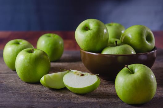Bowl of green apples and slices of apple over wooden board