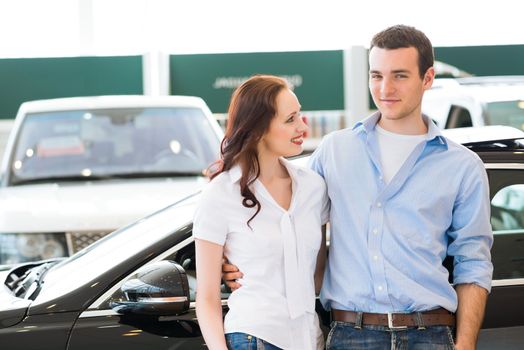 Young couple standing embracing near a car in the showroom