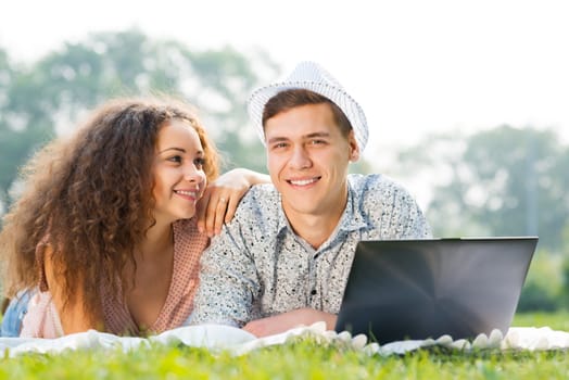 couple lying together in a park, working together on a laptop