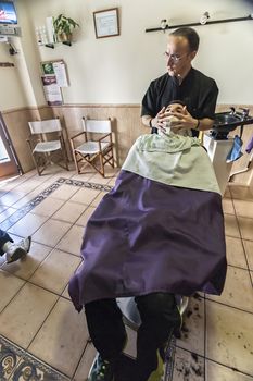 barber applies a hot water cloth in the face of the client to relax the skin in a barber's shop, Sabiote, Jaen province, Andalucia, Spain