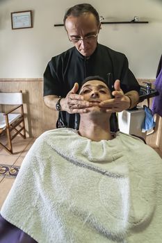 Barbero extends cream in the face of the client after shaver in a barber's shop, Sabiote, Jaen province, Andalucia, Spain