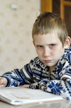 The 10-year-old boy with tears in the eyes sits before the textbook, doing homework