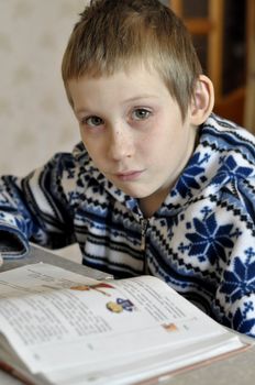 The 10-year-old boy with tears in the eyes sits before the textbook, doing homework