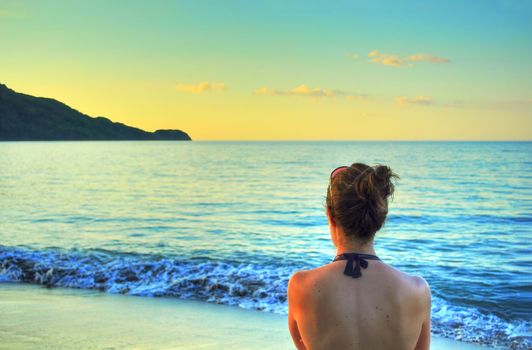 Young woman's back, enjoying the sunset over the sea at the beach in Costa Rica, cyan and yellow tones
