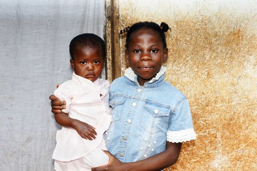 Two black African girls: big or older sister taking care of the family's baby 