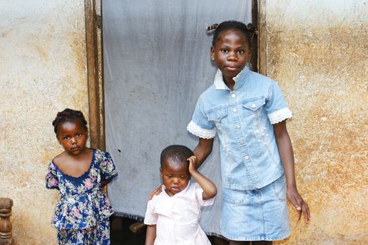 Three black African girls, sisters from a larger family, by their house's doorway