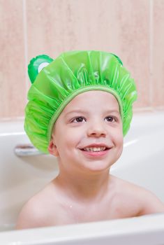 Cute boy happiness with a green cap having bath in bathtub