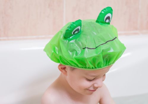 Cute boy happiness with a green cap having bath in bathtub