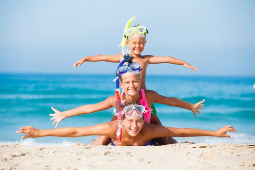 Three happy children on beach with colorful face masks and snorkels, sea in background.