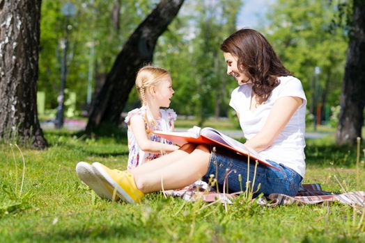 girl with the teacher reading a book together in the summer park