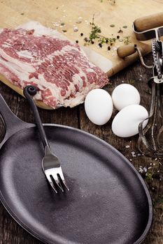 Cast iron skillet with uncooked beef bacon with fresh eggs. 