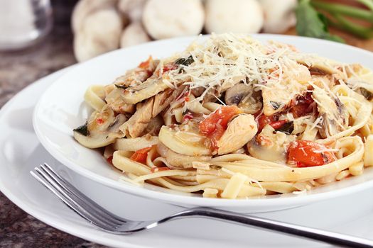 Chicken linguine with grilled chicken, tomatoes, mushrooms and freshly grated parmesan cheese. Fresh mushrooms and herbs in background.
