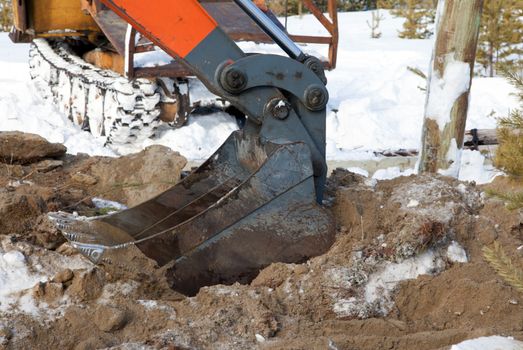 
Bucket hydraulic excavator digging a pit in a snowy forest 
