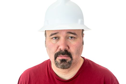Morose glum looking man with a goatee beard wearing a hardhat looking at the camera with lacklustre eyes and a depressed expression, isolated on white