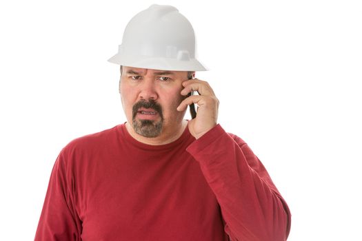 Workman with a goatee beard wearing a hardhat listening to a call on his mobile phone with a look of shocked confusion isolated on white