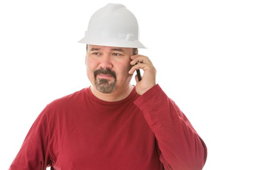 Bored looking workman, engineer or architect chatting on his mobile looking away with a thoughtful wry expression as he listens to the conversation, isolated on white