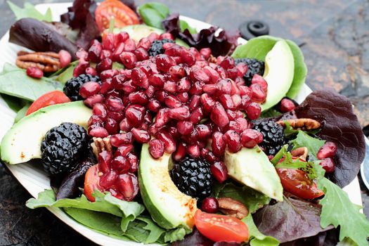 A healthy salad with pomegranate, avocado, tomatoes, almonds and argula lettuce over a rustic background. 