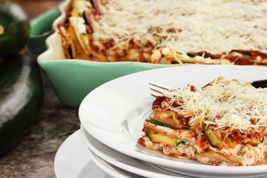 A serving of zucchini lasagna with fresh zucchini and casserole dish in background. 