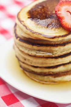 Pancakes, honey and strawberry on checkered fabric