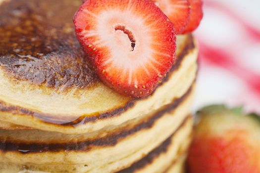 Pancakes, honey and strawberry on checkered fabric