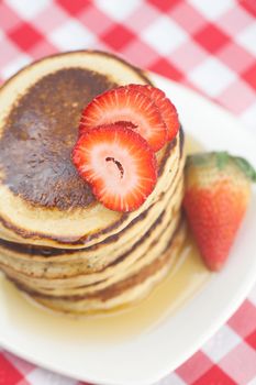 Pancakes, honey and strawberry on checkered fabric