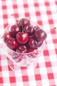 Cherries in a glass bowl on checkered fabric