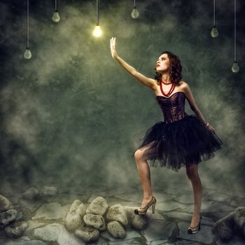 young woman holds up a hand to a glowing light bulb
